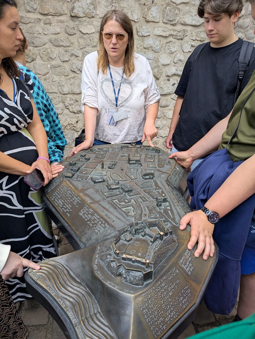 Maquette en bronze en relief de la ville, avec écriture braille ; la guide explique au groupe.