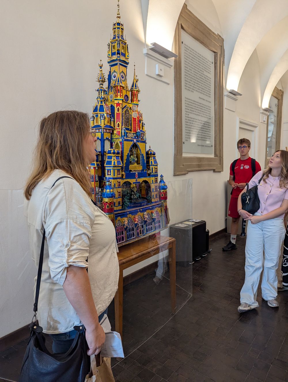 Crèche de Cracovie bleu et or présentée en vitrine ; la guide commente pour le groupe.