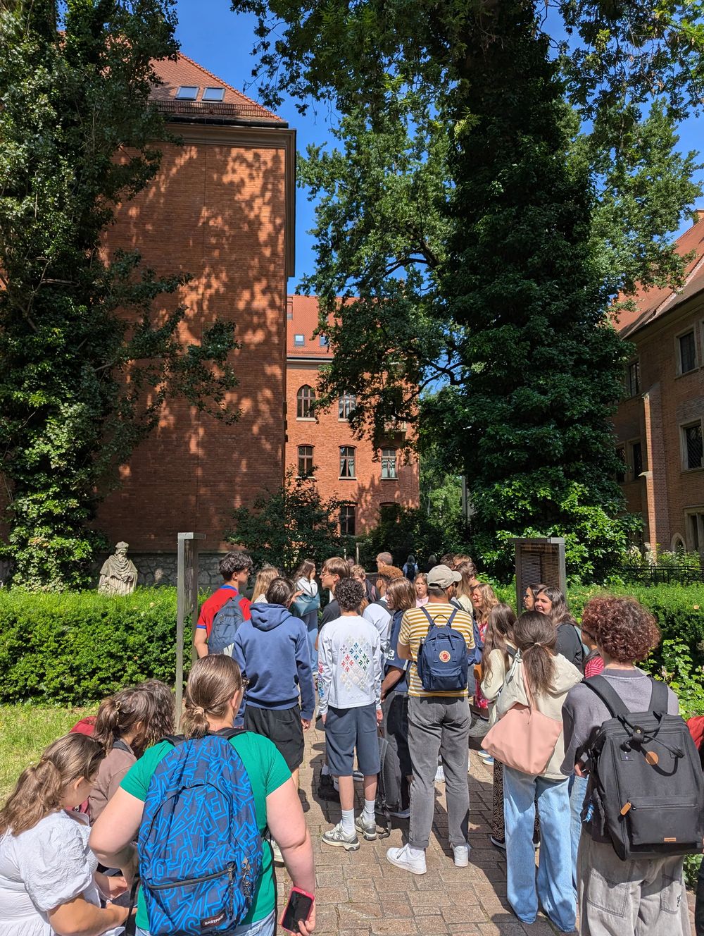 Le groupe dans un jardin verdoyant devant un bâtiment en brique rouge.