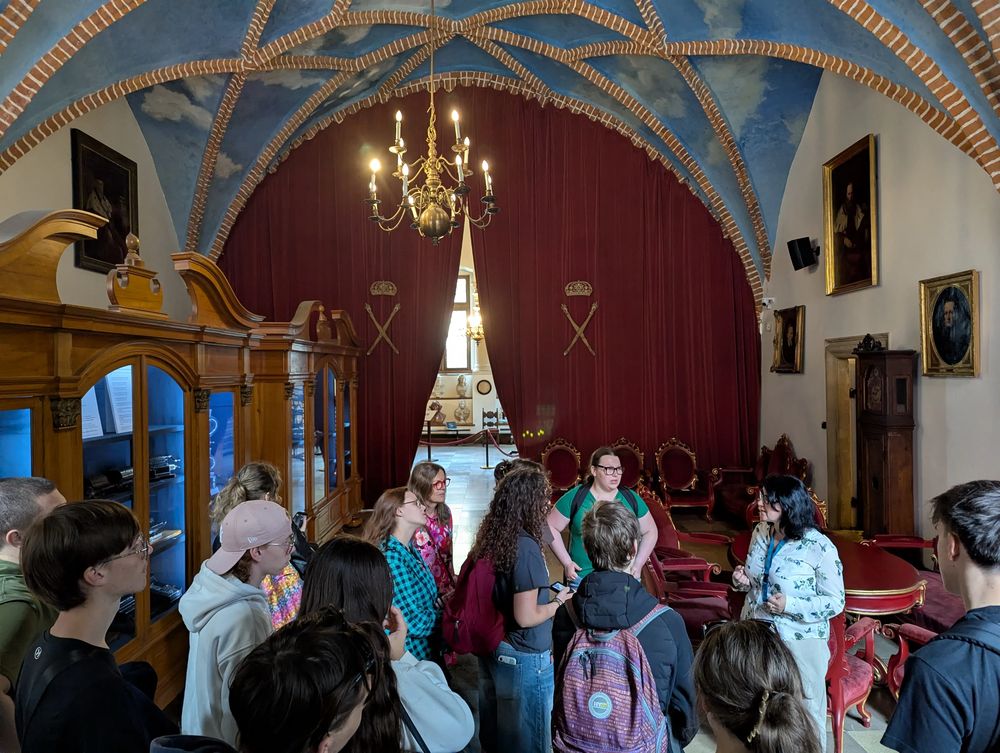 Salle au plafond voûté peint en bleu, lustre doré ; le groupe écoute les explications.