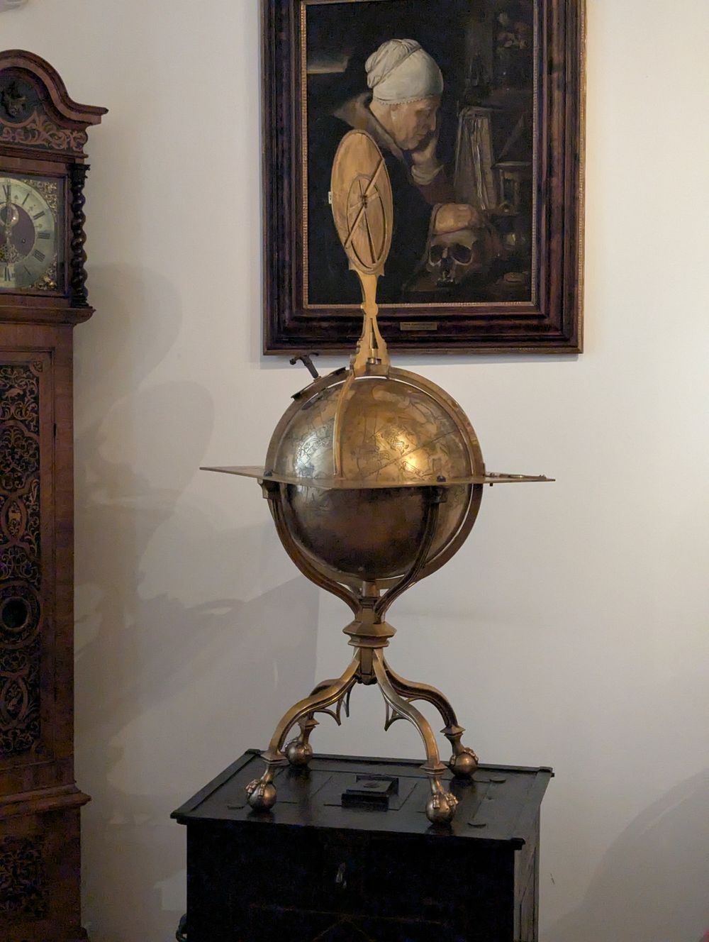 Globe céleste ancien en laiton sur trépied, près d'une horloge et d'un tableau.