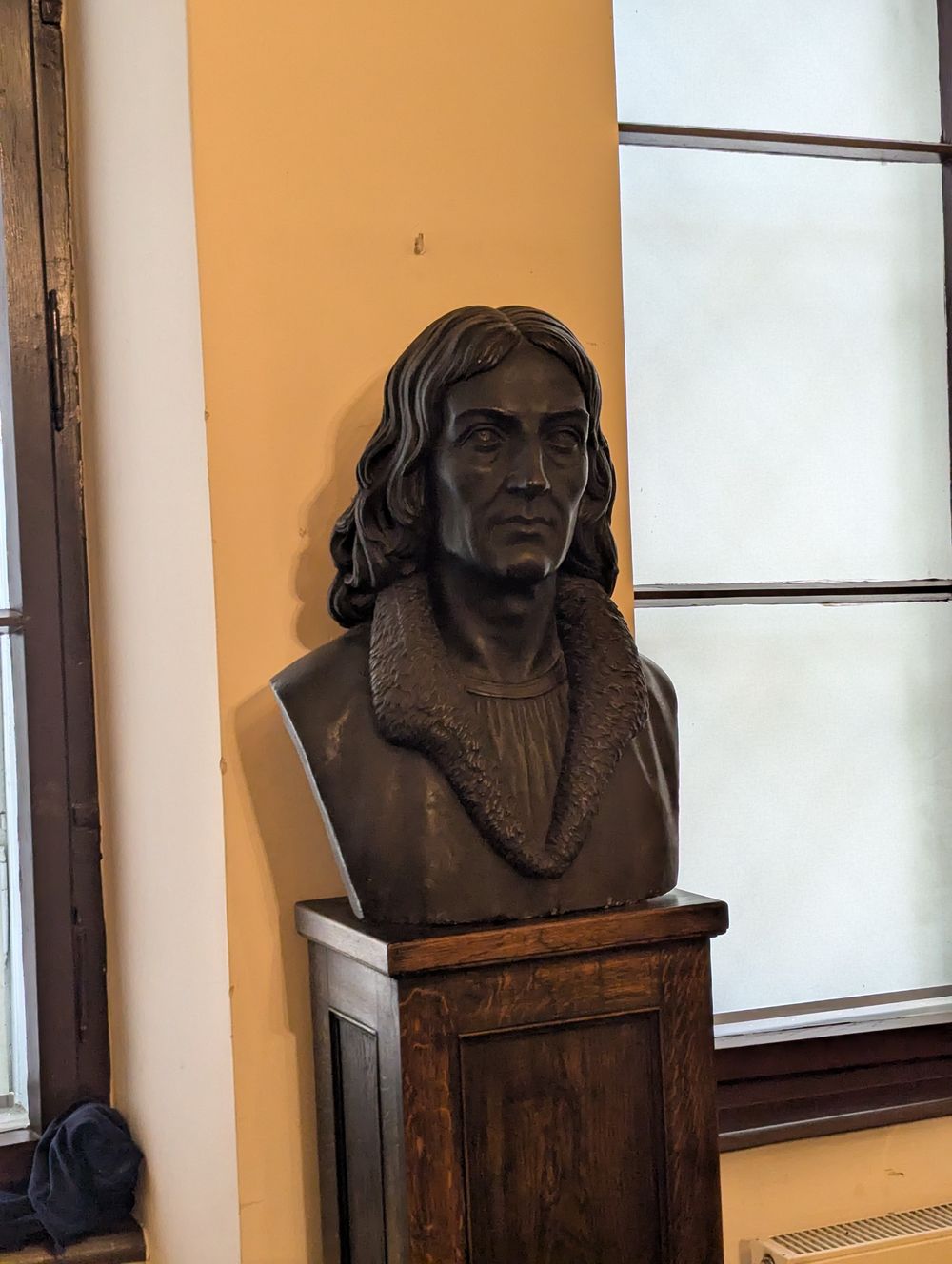 Buste en bronze d'un homme aux cheveux longs, Nicolas Copernic, sur un socle en bois.