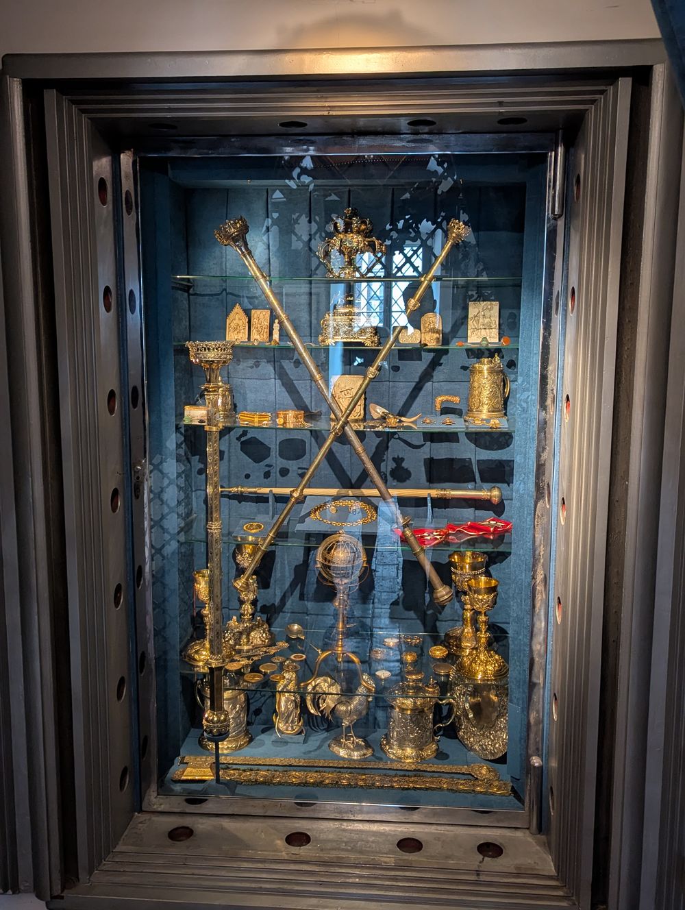 Vitrine blindée remplie d'objets précieux dorés : couronne, sceptres, coupes.