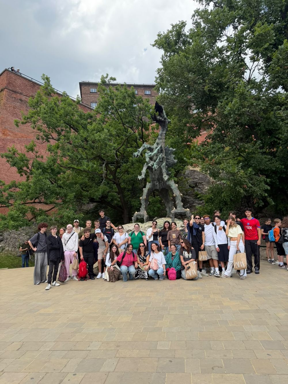 Grande photo de groupe du voyage devant la statue de bronze du dragon de Wawel (Smok Wawelski), au pied du château.