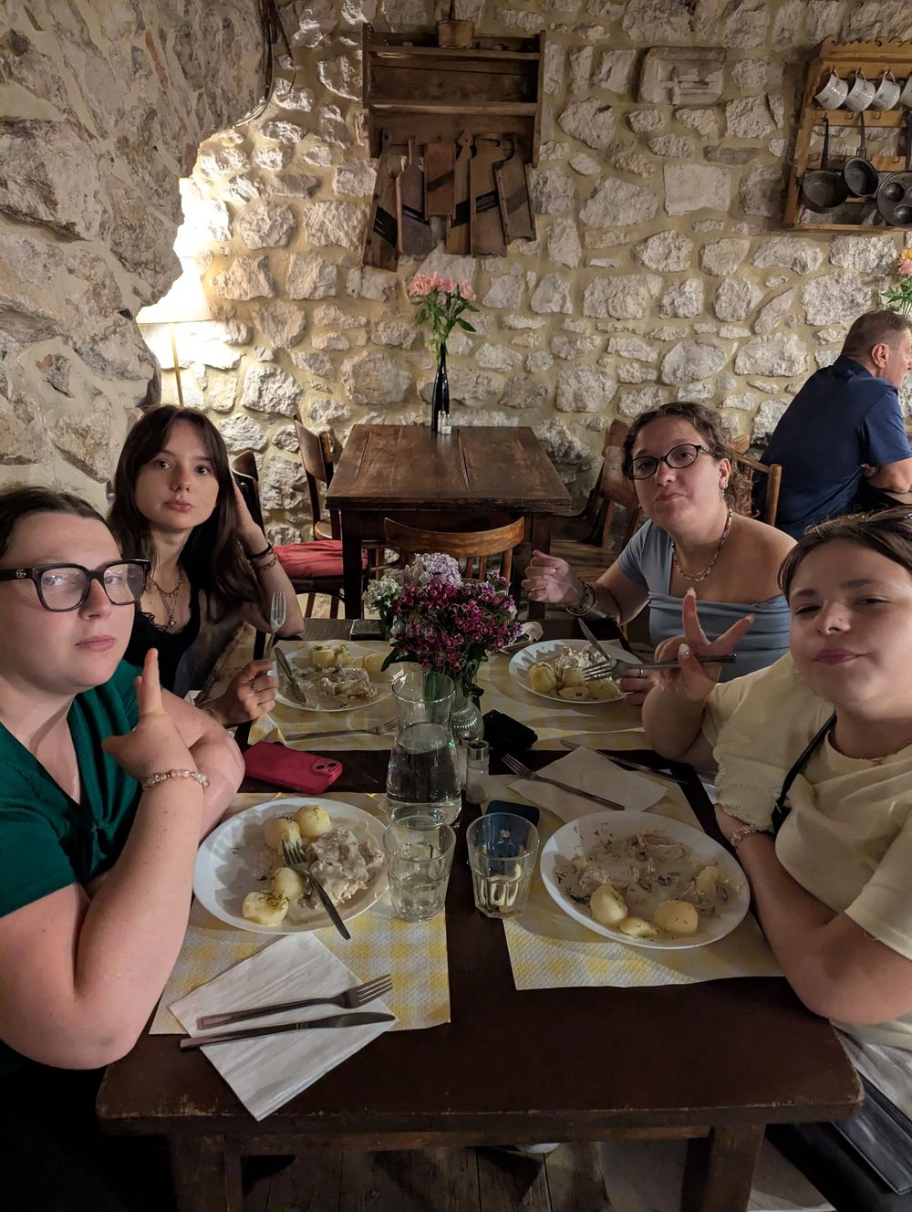 Quatre convives à une table, dans une salle aux murs de pierre, avec assiettes de poulet et pommes de terre.