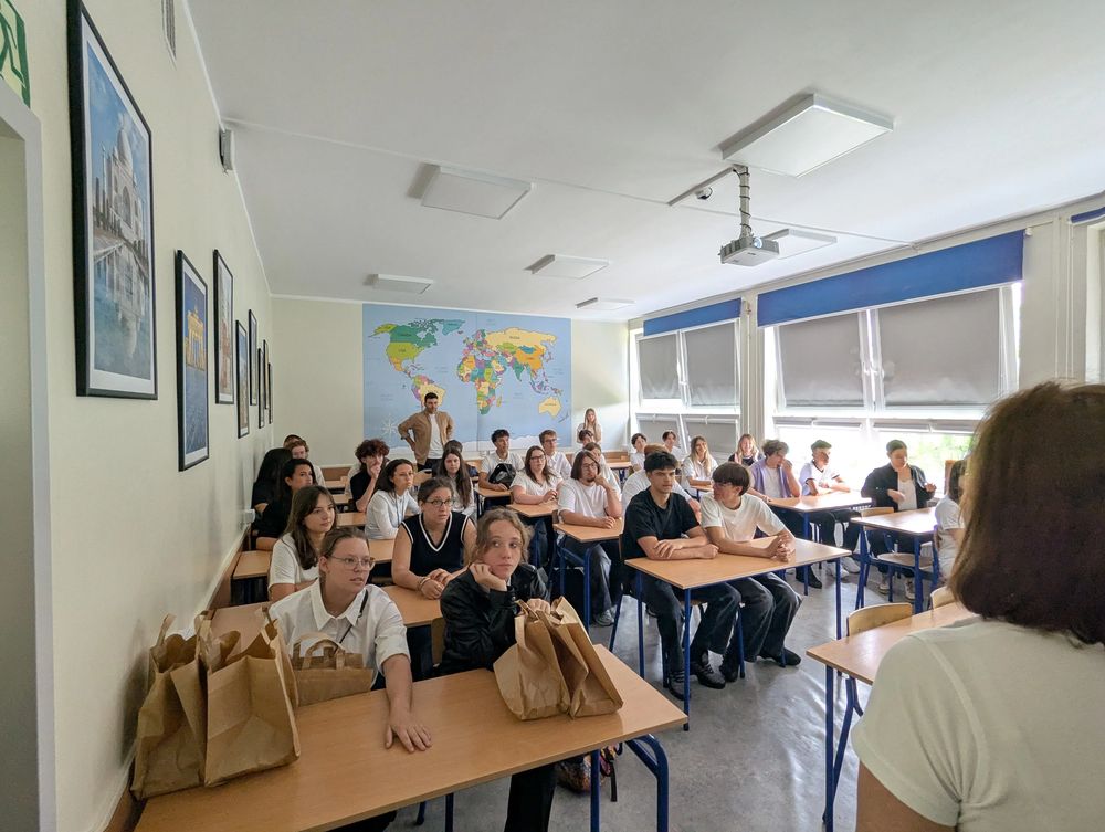 Le groupe assis à des tables, avec des sacs en papier, devant une grande carte du monde.