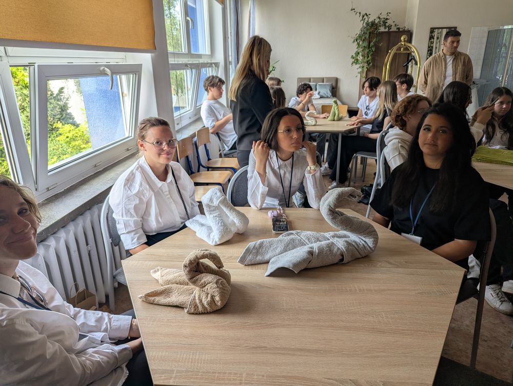 Plusieurs serviettes pliées en forme de cygnes posées sur une table, le groupe assis autour.