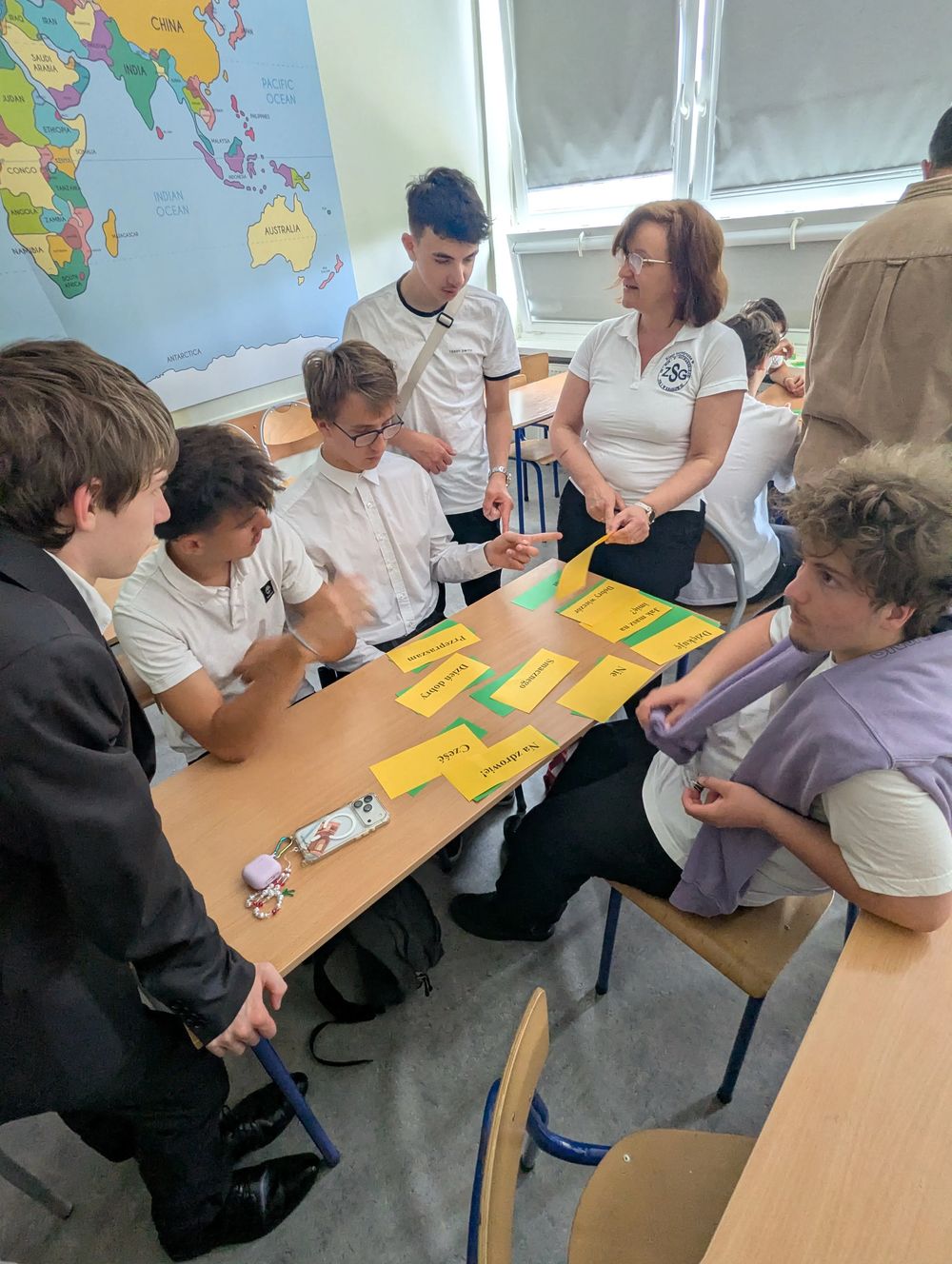 Autour d'une table, des élèves associent des étiquettes de mots polonais et français avec une enseignante.