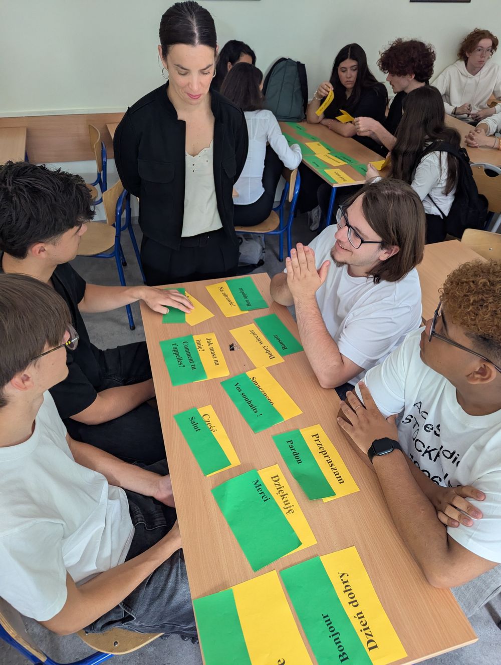 Sur la table, des cartes vertes et jaunes relient des mots français et polonais : Bonjour, Merci, Pardon.