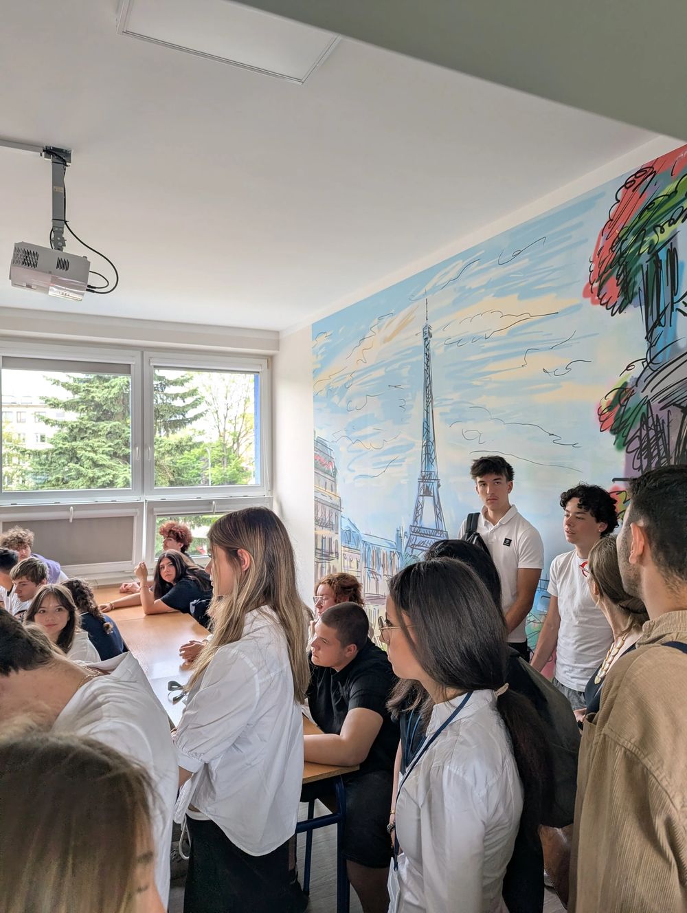 Élèves rassemblés dans une salle de classe ornée d'une fresque de la tour Eiffel et de Paris.