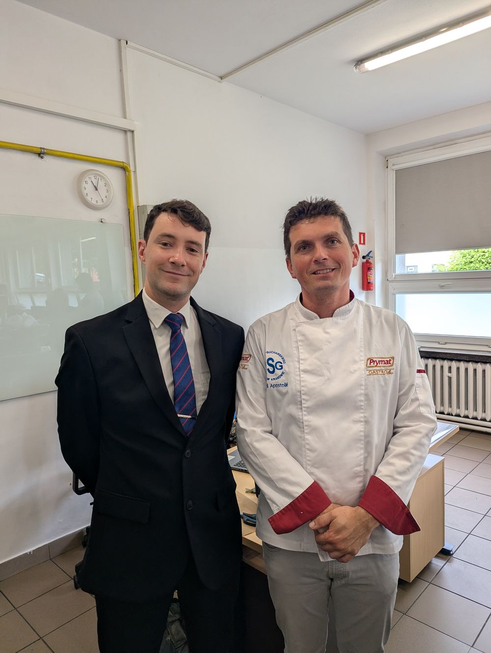 M. Hermand, en costume, pose aux côtés du chef de cuisine de l'école en veste blanche.