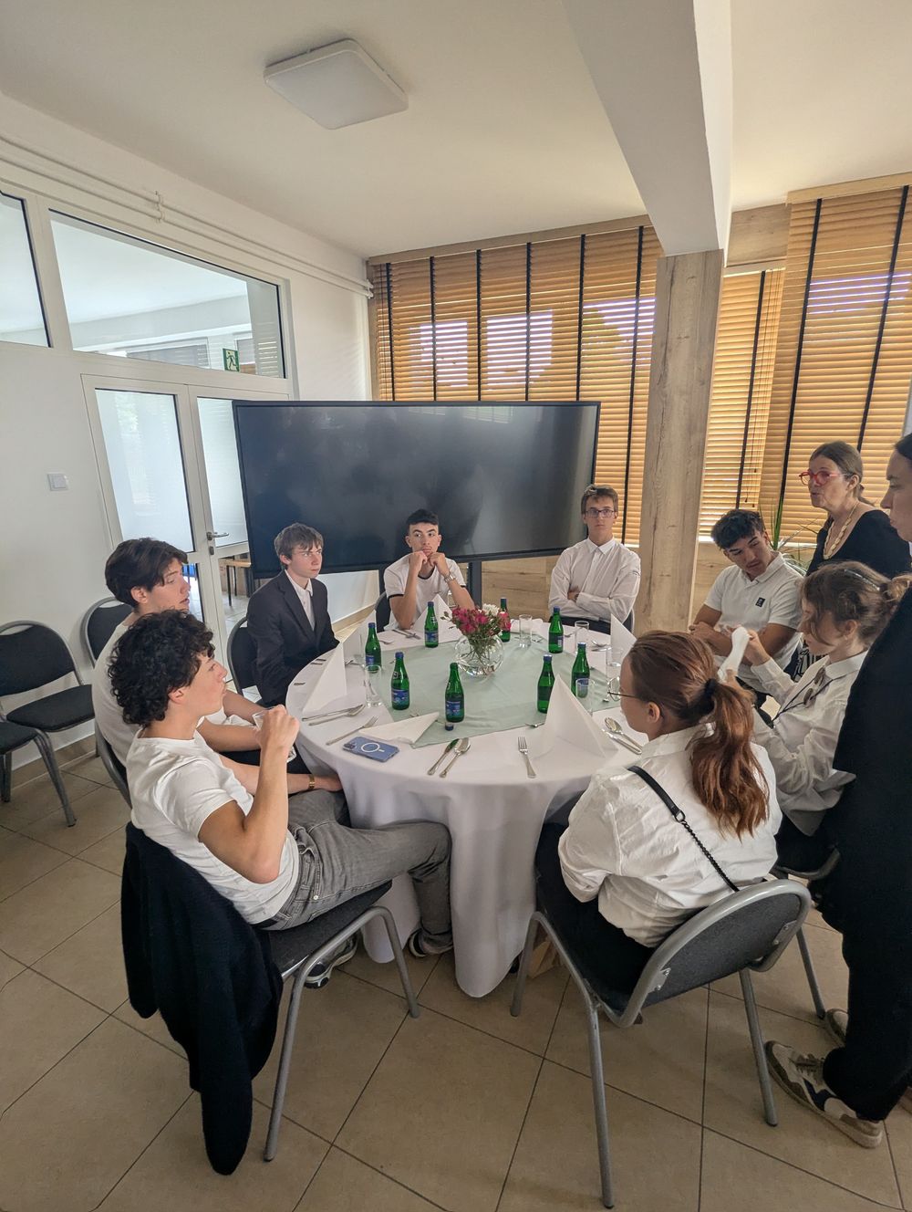 Une table ronde dressée, des convives assis et des élèves serveurs autour.