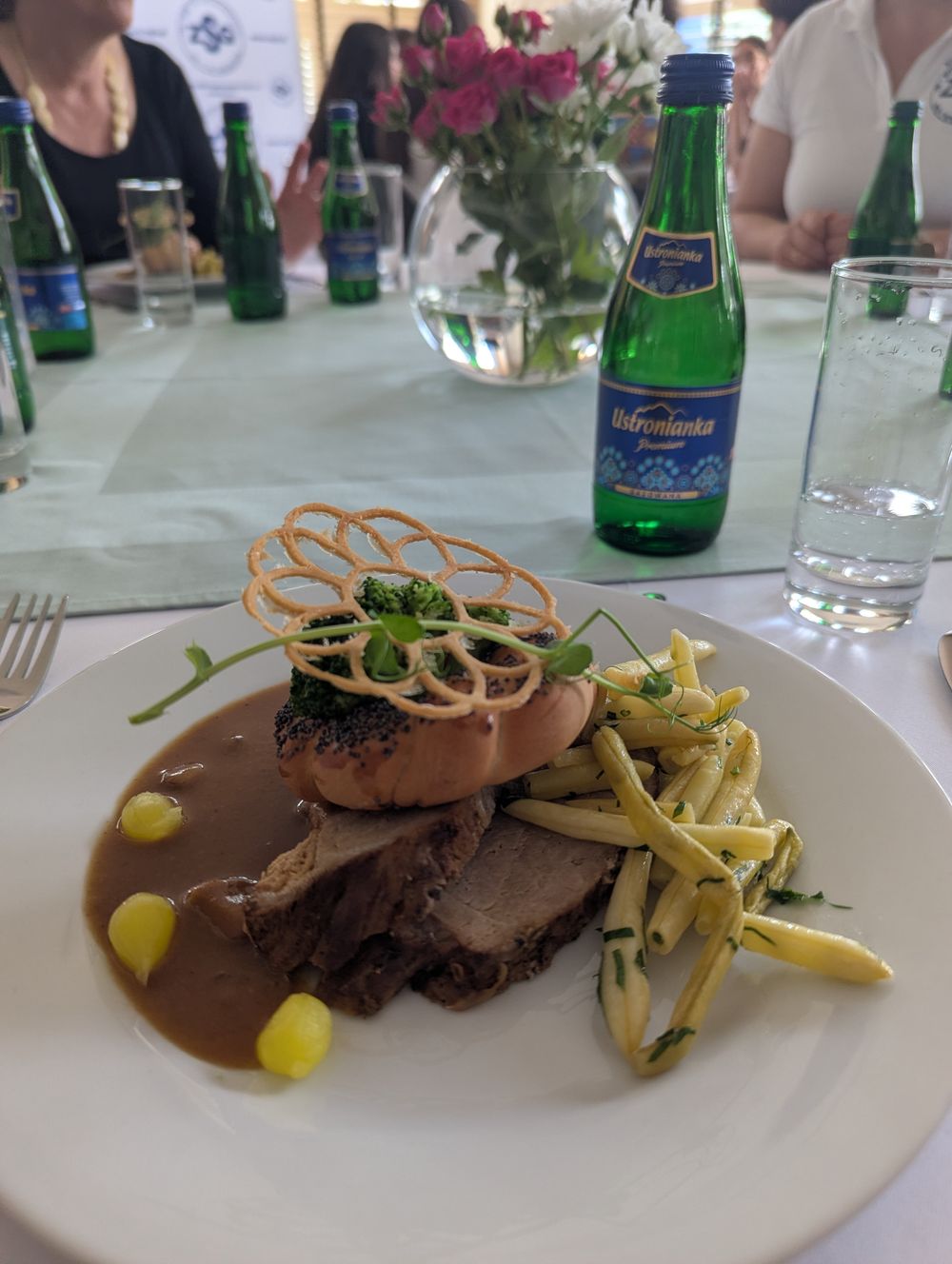 Tranches de porc rôti nappées de sauce, accompagnées d'un petit pain polonais aux graines de pavot et de haricots beurre persillés.