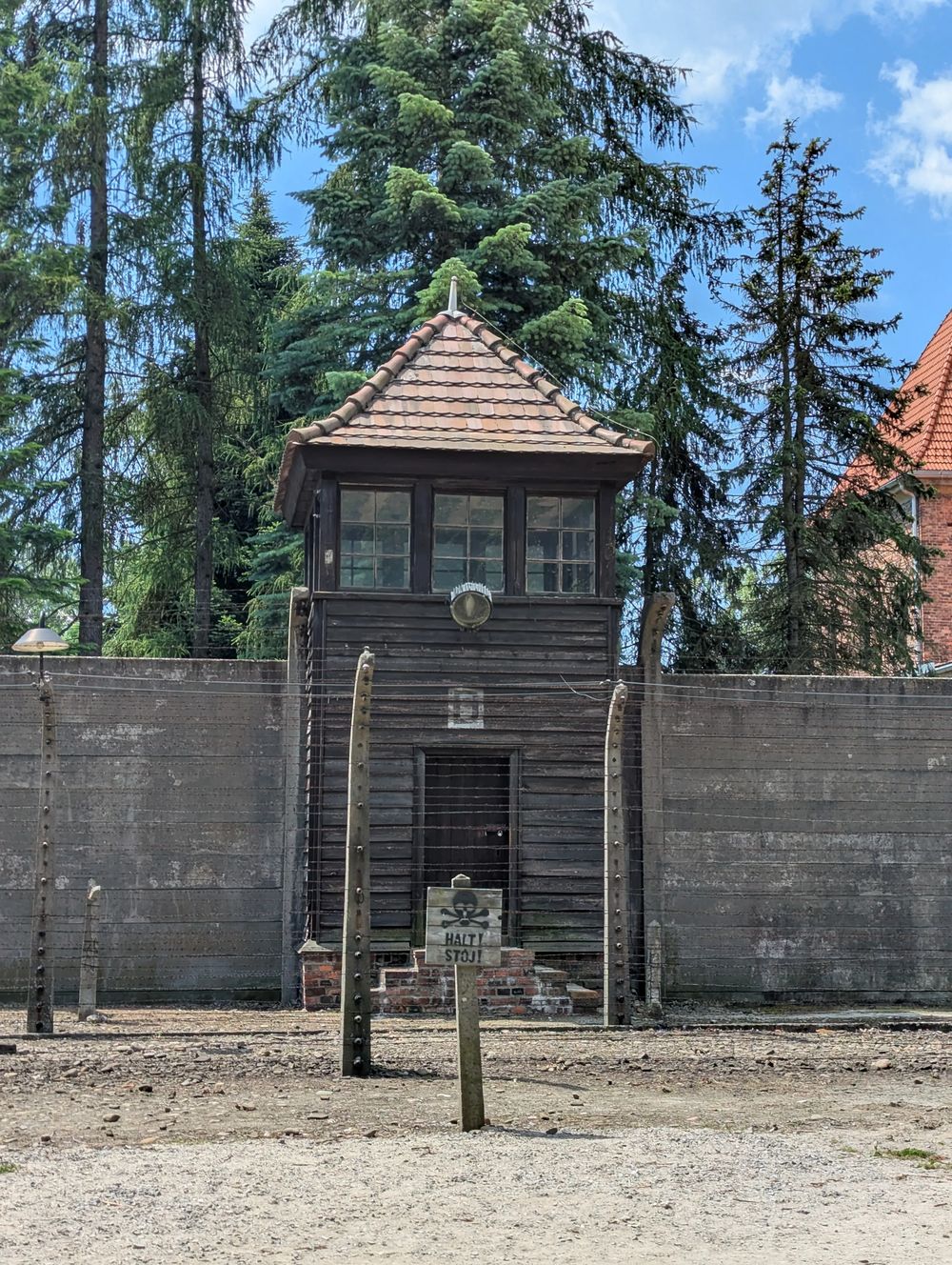 Un mirador en bois et la double clôture de barbelés, avec un panneau d'avertissement « Halt! Stój! ».