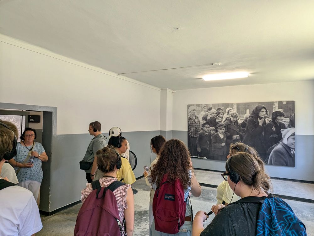 Dans le musée, le groupe écoute la guide devant une grande photographie historique de personnes déportées.