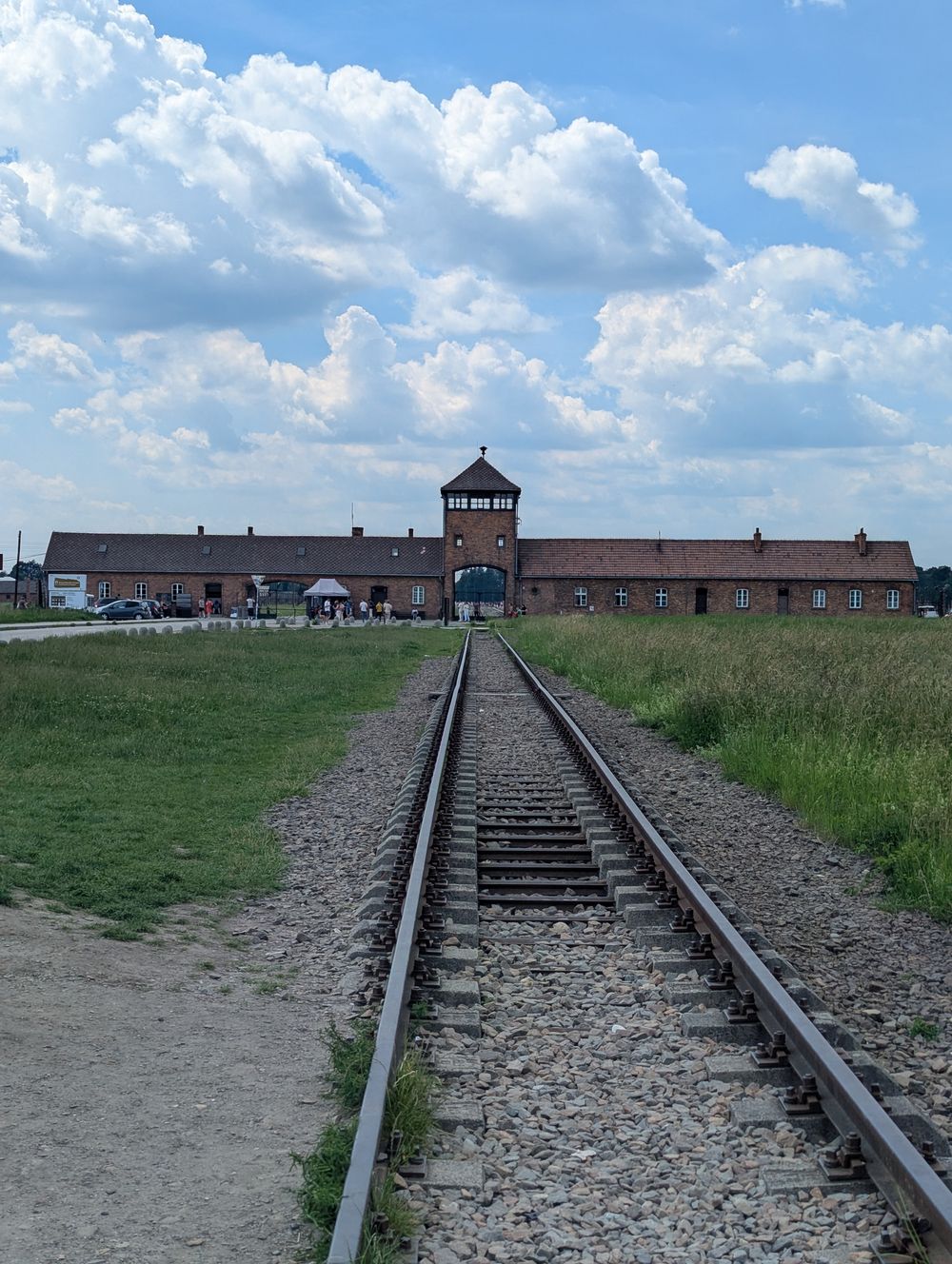 La porte de Birkenau et la voie ferrée qui pénètre dans le camp, sous un grand ciel nuageux.
