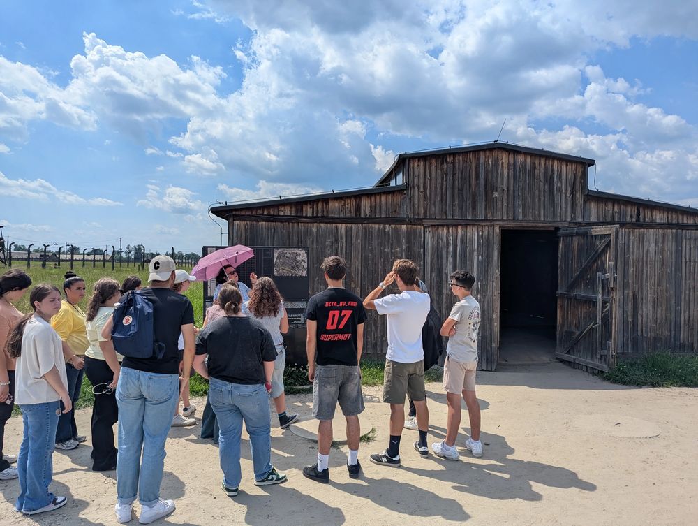 La guide commente devant une baraque en bois de Birkenau, près d'un panneau d'information.