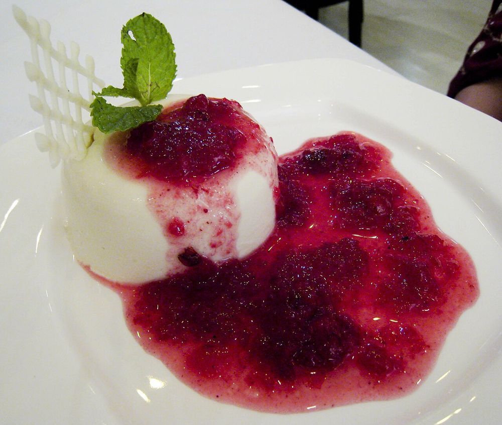 Une panna cotta nappée d'un coulis de fruits rouges, décorée d'une feuille de menthe.